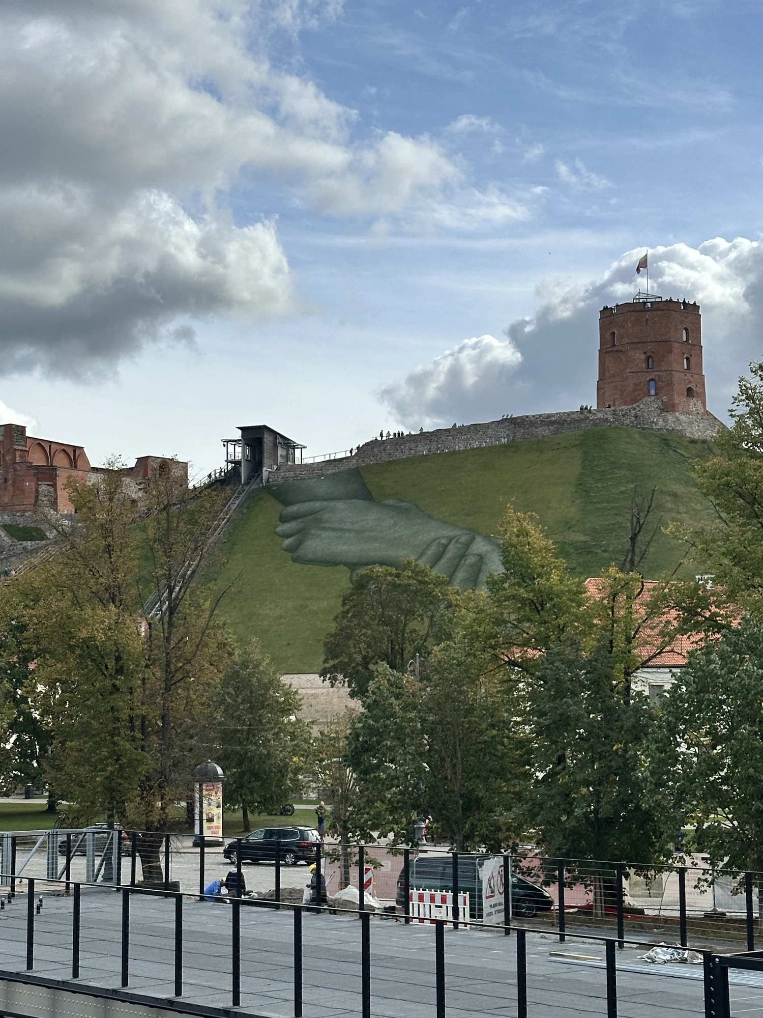 A view of Gediminas' Tower on a grassy hill in Vilnius, featuring a large-scale painting of two clasped hands on the hillside.